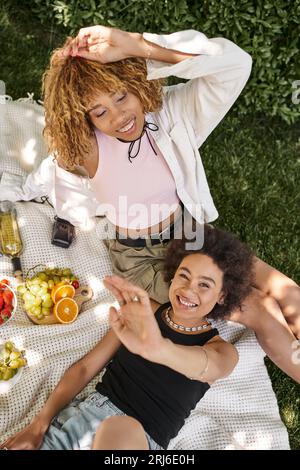 Aufgeregte afroamerikanische Frau, die in der Nähe einer Freundin mit geschlossenen Augen auf die Kamera schaut, Draufsicht Stockfoto