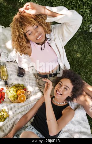 Blick von oben auf die afroamerikanische Frau, die in der Nähe einer Freundin mit geschlossenen Augen lächelt, Spaß im Park Stockfoto