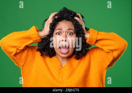 Dunkelhaarige Frau in Orange sieht gestresst und schockiert aus Stockfoto