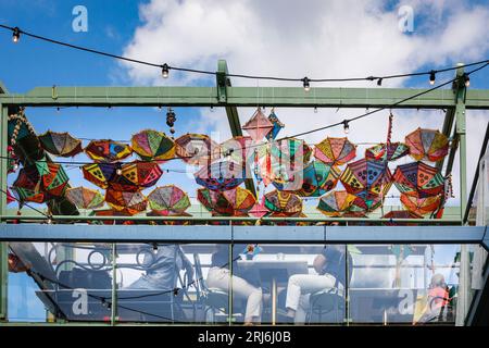 Die Leute sitzen in einem Café mit bunten indischen Regenschirmen, Buck Street Market, Camden Market, Camden Town, London, England Stockfoto