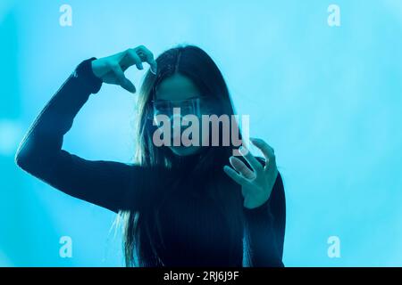 Ein Porträt einer jungen brünetten Frau mit VR-Brille vor blauem Hintergrund Stockfoto