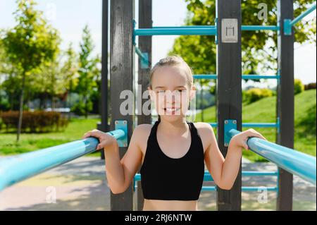 Porträt eines Mädchens in Sportbekleidung in der Nähe der horizontalen Bar und der Turnstangen im Freien. Das Konzept des Sports. Workout. Stockfoto