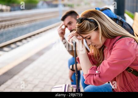 Ein müdes Paar, das am Bahnhof sitzt und auf die Ankunft des Zuges wartet. Stockfoto