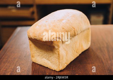 Eine Nahaufnahme eines frisch gebackenen weißen Brotlaibs auf einem Holztisch mit Regalen und Schubladen im Hintergrund Stockfoto