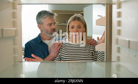 Standpunkt POV von innen Kühlschrank Kaukasisches erwachsenes Paar offen leerer Kühlschrank Frau traurige Verzweiflung Mann beruhigende Ehepartner Familie Arm Reife Stockfoto