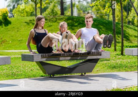 Junge Familie, die bauchmuskeltraining auf einer Parkbank macht. Mutter Vater und Tochter pumpende Presse im Park. Stockfoto