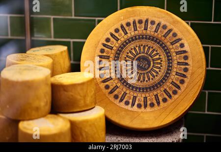 Eine Szene mit verschiedenen Käsesorten, die auf Holztellern serviert werden, vor einem Hintergrund mit grün und blau gefliesten Wänden Stockfoto