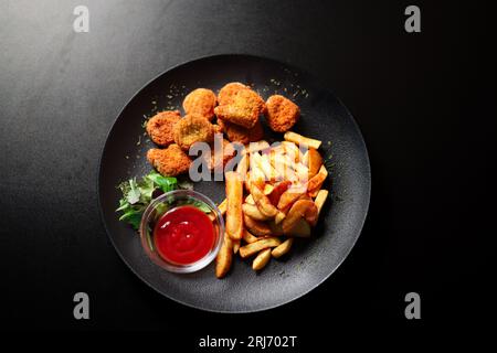 Eine Nahaufnahme eines Teller mit goldbraunen Hähnchennuggets und Pommes frites auf schwarzem Hintergrund Stockfoto