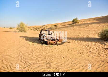Verbranntes Autowrack auf einer Spur in der Wüste zwischen den Dünen mit blauem Himmel Stockfoto