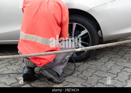 Salvador, Bahia, Brasilien - 11. August 2023: Ein Tankstellenarbeiter wird gesehen, wie er einen Autoreifen auf der Avenida Tancredo Neves aufpumpt. Stadt Salvador, Bahia. Pumpe Stockfoto