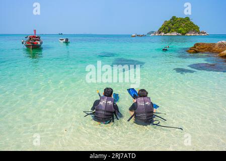 Ko Lipe, Thailand - 11. April 2023: Zwei Personen sitzen im flachen Meerwasser in Schwimmwesten mit Schnorchelausrüstung am Sunrise Beach. Stockfoto