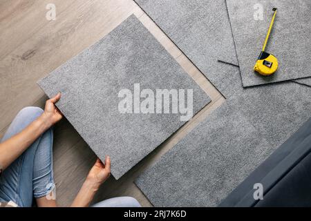 Frau, die Teppichfliesen im Wohnzimmer auf den Boden legt. heimwerkerbedarf Stockfoto