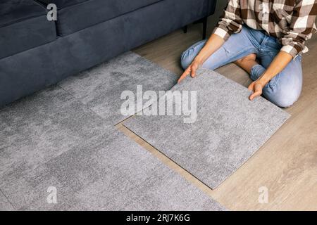 Frau, die selbstklebende Teppichfliesen auf den Boden im Wohnzimmer zu Hause legt Stockfoto