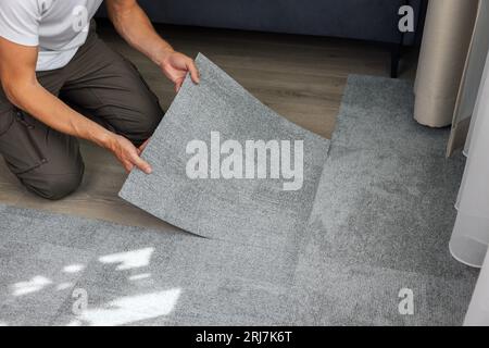 Mann, der selbstklebende Teppichfliesen auf dem Boden im Wohnzimmer zu Hause installiert Stockfoto