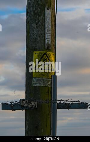 Telefonstange mit Gefahrenschild und Stacheldraht. Stockfoto