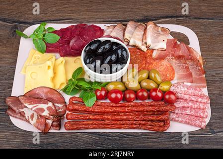 Oliven, grünes Basilikum und Teile von Käse, Würstchen und Fleischprodukten. Snacks auf einem Servierbrett. Stockfoto