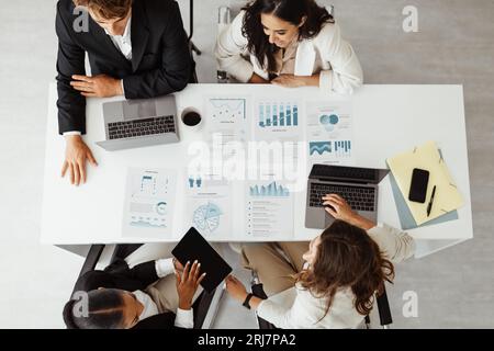 Konferenzraum für Startups. Geschäftsleute sitzen am Tisch, verwenden Laptops und teilen Dokumente mit Statistiken, Draufsicht Stockfoto