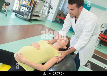 Physiotherapeutin, die lächelnde Schwangere in der Turnhalle trainieren lässt Stockfoto