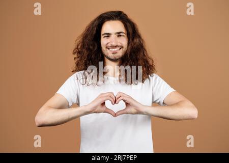 Mann mit langen Haaren, die die Hände zum Herzen machen, Studio Portrait Stockfoto
