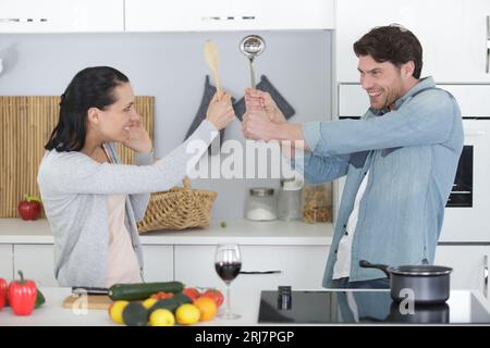 Komisches Paar, das beim Kochen so tut, als würde es sich mit Utensilien streiten Stockfoto