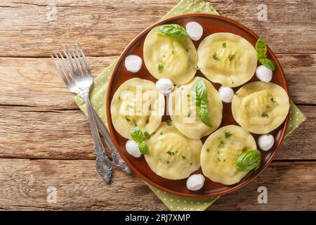 Cappellacci frisch gefüllte Pasta mit köstlichem Mozzarella und Basilikum auf dem Teller auf dem Holztisch. Horizontale Draufsicht von A Stockfoto