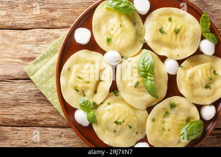 Leckere italienische Cappellacci-Knödel mit Mozzarella und Basilikum auf dem Teller auf dem Holztisch. Horizontale Draufsicht von oben Stockfoto