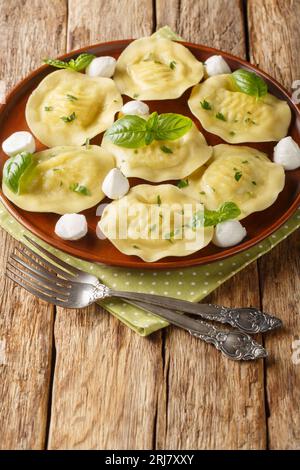 Italienische Pasta Cappellacci Mozzarella mit Basilikum-Nahaufnahme auf dem Teller auf dem Holztisch. Vertikal Stockfoto