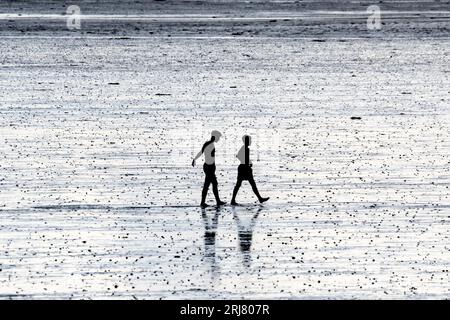 Silhouette von zwei Jungen, die bei Ebbe über den Strand von Snettisham am Ufer des Waschbads laufen. Stockfoto