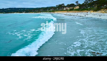 Wellenschlag gegen Carmel Beach mit Menschen, die auf der sandigen Uferantenne wandern Stockfoto