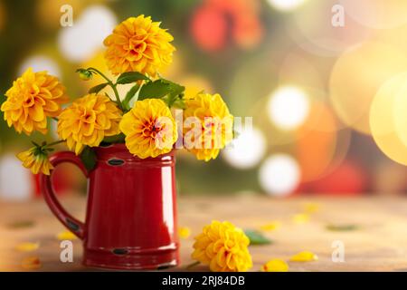 Herbstlicher Blumenstrauß aus frischer gelber Dahlie in Vintage-Rotkrug auf unscharfem grünem Hintergrund mit festlichem Bokeh. Stockfoto