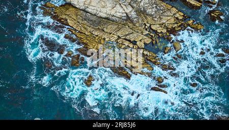 Abwärts gerichtete Ansicht von Wellen, die auf teilweise untergetauchte Felsen entlang  stürzen Stockfoto
