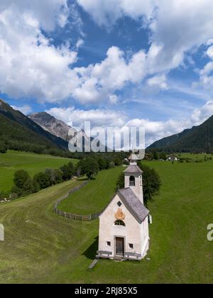 Kleine weiße Alpenkapelle auf grünem Grasfeld im Tal zwischen felsigen Almgipfeln in den italienischen Dolomiten Stockfoto