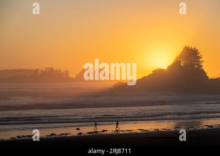 Die Silhouetten der Leute laufen am Cox Bay Beach bei Sonnenuntergang auf Vancouver Island, British Columbia, Kanada. Stockfoto