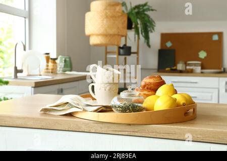 Tablett mit Zimtrollen, Tassen, Zitronen und Teeblättern auf Holzarbeitsplatte in der modernen Küche Stockfoto