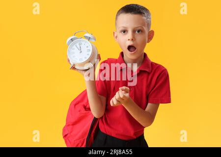 Überraschter Schuljunge mit Wecker auf gelbem Hintergrund Stockfoto