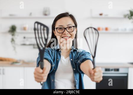 Asiatische Frau zeigt Küchengeräte, während sie drinnen steht Stockfoto