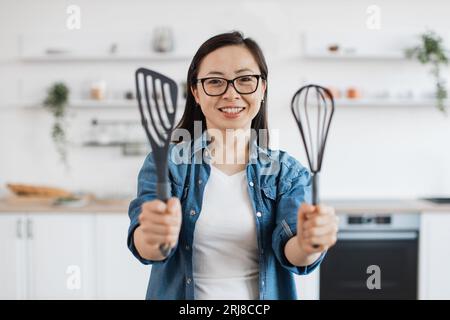 Asiatische Frau zeigt Küchengeräte, während sie drinnen steht Stockfoto