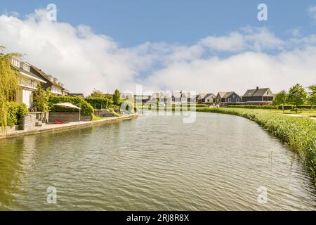 Ein Fluss mit Häusern und Bäumen im Hintergrund an einem sonnigen Tag, vom Ufer aus gesehen Stockfoto