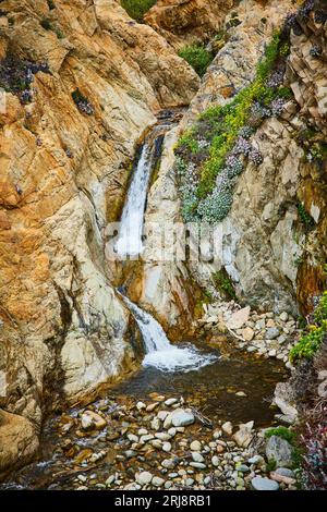 Kleiner Bach zwischen Felswänden, der in ein seichtes Becken mit großen Steinen fließt Stockfoto