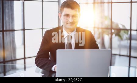 Attraktiver Geschäftsmann in einem eleganten schwarzen Anzug an einem Laptop Stockfoto