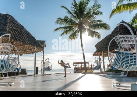 Eine junge Frau steht anmutig auf einem Bein in einem hellen Stuhl mit offenem und luftigem Design Stockfoto