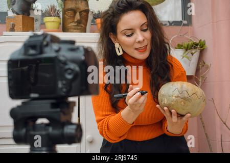Erwachsene Frau zu Hause in oranger Kleidung, konzentrierte Malerei Kürbis mit Augen und Mund, um es für halloween zu dekorieren, People Concept, Copy sp Stockfoto
