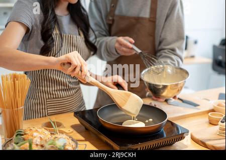 Abgeschnittenes Bild eines hübschen Paares, das gemeinsam in einer minimalistischen Küche Pfannkuchen zubereitet. Kochtermine zu Hause, Freizeit, Familienaktivitäten Stockfoto