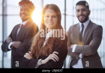 Drei multiethnische Arbeiter in formellen Anzügen, die drinnen vor der Kamera stehen und lächeln. Stockfoto