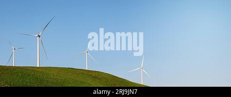 Banner mit Windkraftanlagen auf dem grünen Hügel über dem blauen Himmel. Nachhaltiger Energiehintergrund Stockfoto