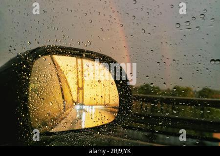 Nahaufnahme des Rückspiegels mit Sonnenuntergang und Regenbogen und Regentropfen auf dem Glas Stockfoto