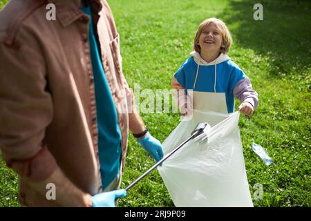 Porträt eines glücklichen kleinen Jungen, der sich freiwillig mit seinem Vater in der Natur engagiert und gemeinsam Müll aufnimmt Stockfoto