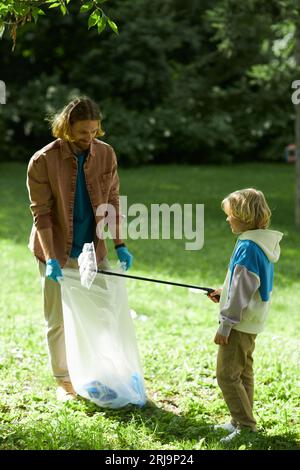 Ein Portrait von Vater und Sohn als Öko-Freiwillige, die im Sommerpark Müll sammeln Stockfoto