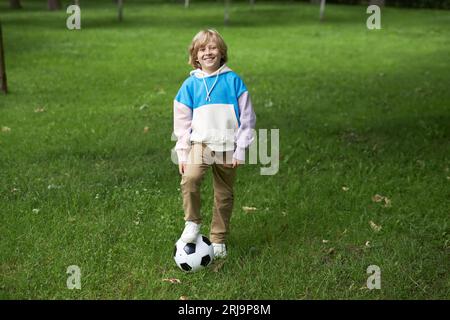 Porträt in voller Länge von lächelndem Tween Boy mit Fußballball im Freien, der auf grünem Gras steht, Kopierraum Stockfoto