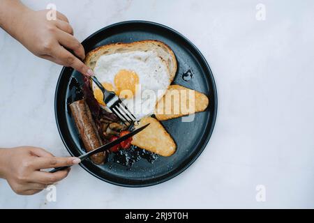 Flache Lage oder Draufsicht und selektiver Fokusschuss von den Händen zerteilt den Sauerteig auf einem Teller voll englisches Braten Frühstücksmenü auf isoliertem weißem bac Stockfoto